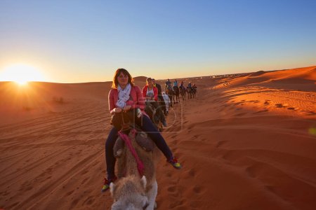 Téléchargez les photos : Un groupe de touristes joyeux embarque sur un safari chameau, explorant le désert du Sahara enchanteur au Maroc - en image libre de droit