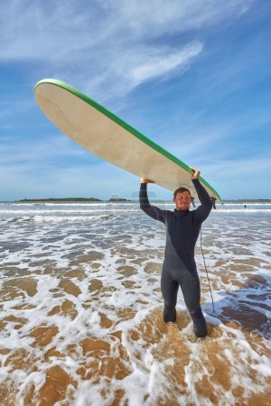 Téléchargez les photos : Un jeune surfeur pose avec sa planche au bord de l'océan à Essaouira, capturant l'essence de la culture du surf dans le cadre pittoresque de l'Atlantique - en image libre de droit
