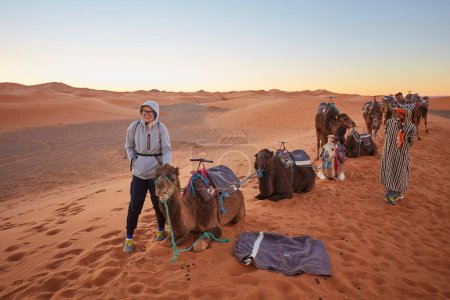 Téléchargez les photos : Vivez la tranquillité du désert du Sahara pendant que les touristes profitent d'une délicieuse randonnée à dos de chameau à travers ses dunes envoûtantes au Maroc. - en image libre de droit