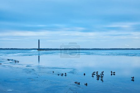 Foto de Una encantadora escena de invierno con un tranquilo embalse, vibrante hielo azul y un faro solitario. - Imagen libre de derechos