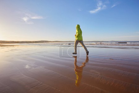 Foto de Un joven con una chaqueta verde disfruta de una carrera a lo largo de la costa de Essaouira en Marruecos, donde la brisa del océano vigoriza la atmósfera costera - Imagen libre de derechos