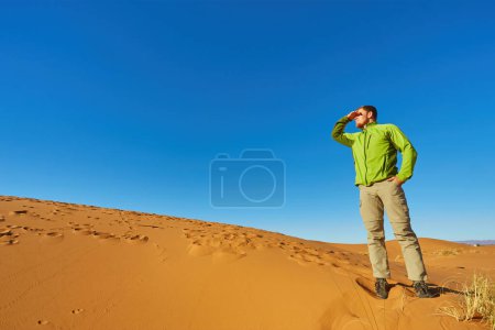 Téléchargez les photos : Un voyageur solitaire se tient parmi les dunes infinies du Sahara, où le sable doré rencontre l'horizon sous le soleil chaud. - en image libre de droit