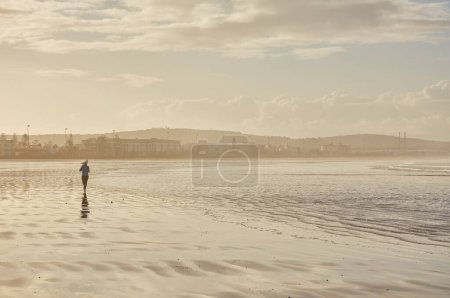 Foto de Una joven mujer abraza la tranquilidad de una carrera junto al mar a lo largo del océano de Essaouira, donde las olas rítmicas crean un relajante telón de fondo para su vigorizante trote - Imagen libre de derechos