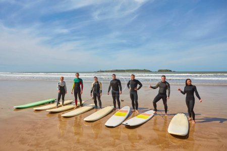 Photo for A group of vibrant young surfers captures a collective moment with their boards on the ocean's edge in Essaouira, Morocco. The camaraderie of surf culture against the backdrop of Essaouira's scenic coastal charm - Royalty Free Image