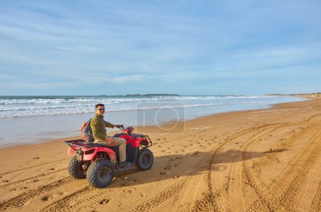 Téléchargez les photos : Un jeune homme explore le front de mer sur un quad près d'Essaouira, capturant le frisson d'une balade aventureuse le long du paysage côtier pittoresque. - en image libre de droit