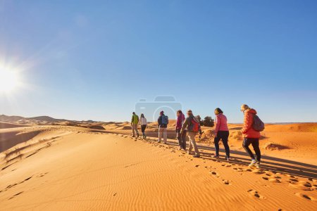 Photo for A group of tourists enjoying a sunny day trekking through the mesmerizing sand dunes of the Sahara Desert in Morocco, capturing the essence of the vast and awe-inspiring landscape - Royalty Free Image