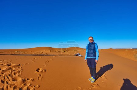 Photo for A lone traveler stands among the endless Sahara dunes, where golden sands meet the horizon under the warm sun. - Royalty Free Image