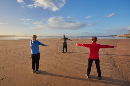 Photo for Young adults energize their day with a group workout by the ocean in Essaouira. The coastal ambiance of Morocco's Essaouira frames their invigorating morning routine - Royalty Free Image