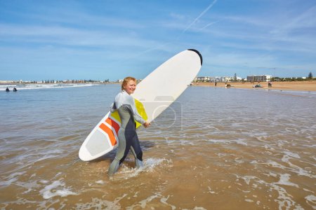 Téléchargez les photos : Une jeune surfeuse pose avec sa planche sur le front de mer d'Essaouira, incarnant une fusion gracieuse de culture du surf et de charme côtier. - en image libre de droit