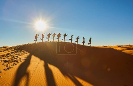 Téléchargez les photos : Un groupe de touristes capture des moments joyeux, pose ludique frappante, silhouette dans le contexte fascinant du désert du Sahara. Maroc. - en image libre de droit