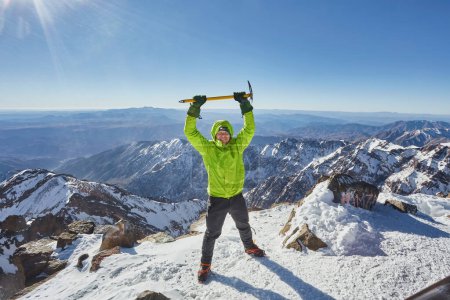Téléchargez les photos : Escalade ou alpiniste au sommet d'une montagne. Un succès de l'alpiniste atteignant le sommet. Sports d'aventure en plein air en hiver paysage montagneux alpin. Journée ensoleillée et un grimpeur sur un sommet d'un pic. - en image libre de droit