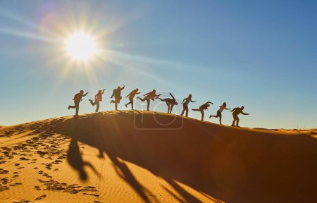 Foto de Los turistas disfrutan de momentos lúdicos en el desierto del Sahara, capturando la risa y la alegría en medio de los cautivadores paisajes. Silueta contra los tonos cálidos del sol poniente. - Imagen libre de derechos