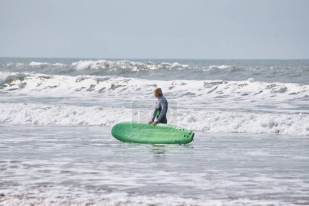 Téléchargez les photos : Une jeune surfeuse pose avec sa planche sur le front de mer d'Essaouira, incarnant une fusion gracieuse de culture du surf et de charme côtier. - en image libre de droit