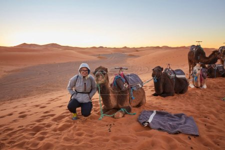 Foto de Experimente la tranquilidad del desierto del Sahara mientras los turistas disfrutan de una deliciosa caminata en camello a través de sus fascinantes dunas en Marruecos. - Imagen libre de derechos