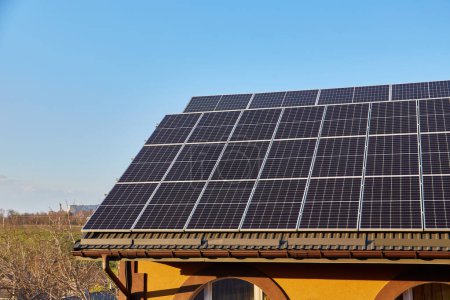 Téléchargez les photos : Panneaux solaires sur petit toit de maison en bois, concept d'énergie durable. Beaucoup d'espace de copie sur ciel bleu clair. - en image libre de droit
