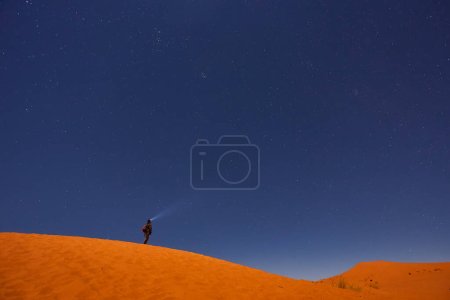 Téléchargez les photos : Un explorateur solitaire, guidé par une lanterne, se lance dans un voyage céleste sous le ciel nocturne du désert, captivé par les merveilles cosmiques au-dessus de lui - en image libre de droit