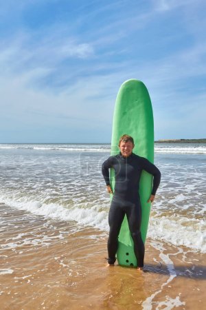 Téléchargez les photos : Un jeune surfeur pose avec sa planche au bord de l'océan à Essaouira, capturant l'essence de la culture du surf dans le cadre pittoresque de l'Atlantique - en image libre de droit