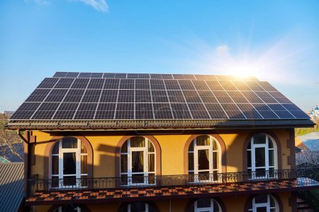Téléchargez les photos : Panneaux solaires sur petit toit de maison en bois, concept d'énergie durable. Beaucoup d'espace de copie sur ciel bleu clair. - en image libre de droit