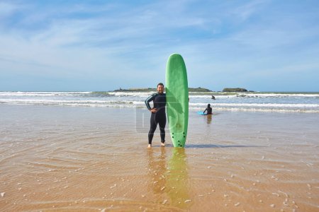 Téléchargez les photos : Un jeune surfeur pose avec sa planche au bord de l'océan à Essaouira, capturant l'essence de l'aventure balnéaire et de la culture du surf. - en image libre de droit