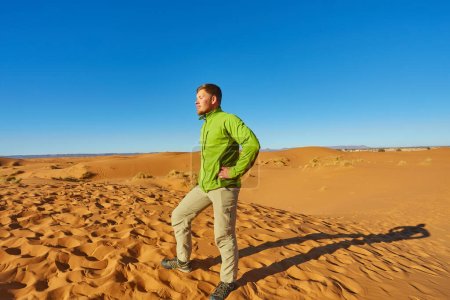 Téléchargez les photos : Un voyageur solitaire se tient parmi les dunes infinies du Sahara, où le sable doré rencontre l'horizon sous le soleil chaud. - en image libre de droit