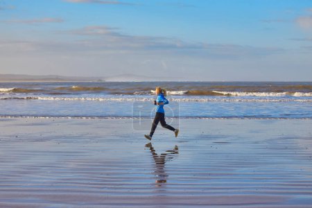 Foto de Una joven disfrutando de un trote costero a lo largo de la costa de Essaouira, con las olas del Atlántico proporcionando un sereno telón de fondo para su vigorizante carrera - Imagen libre de derechos