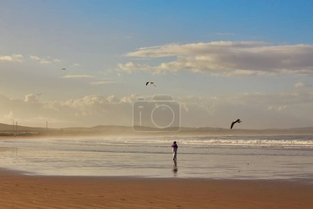 Foto de Una joven mujer abraza la tranquilidad de una carrera junto al mar a lo largo del océano de Essaouira, donde las olas rítmicas crean un relajante telón de fondo para su vigorizante trote - Imagen libre de derechos