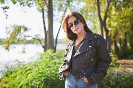 A young brunette, adorned in a leather jacket, poses against the backdrop of nature's breathtaking beauty.