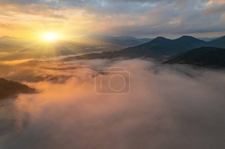 Téléchargez les photos : Brouillard matinal incroyable dans les montagnes. Belle lumière du lever du soleil brille sur la forêt de hêtres rouges. Panorama de drones. Photographie de paysage - en image libre de droit
