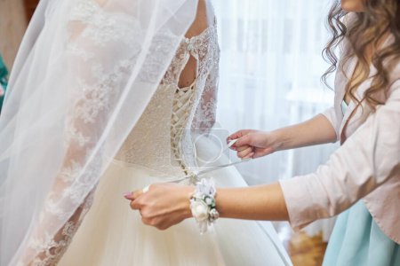 Téléchargez les photos : Aider la mariée à mettre sa robe de mariée - en image libre de droit