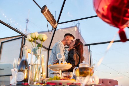 Foto de Una pareja comparte un momento tierno en una azotea, sus siluetas grabadas en el cielo de la noche. El resplandor de la ciudad realza la atmósfera romántica. - Imagen libre de derechos