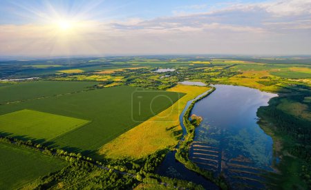 Foto de Vista aérea del amplio río que fluye tranquilamente en el campo rural entre campos verdes en la noche de verano - Imagen libre de derechos