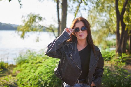 Photo for A young brunette, adorned in a leather jacket, poses against the backdrop of nature's breathtaking beauty. - Royalty Free Image