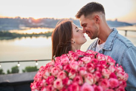 Téléchargez les photos : Jeune couple avec un bouquet de roses sur le fond du coucher de soleil - en image libre de droit