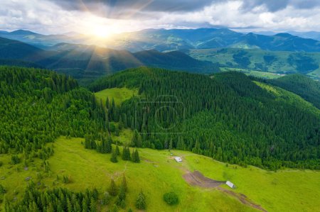 Scenic aerial view of the foggy Carpathian mountains, village and blue sky with sun and clouds in morning light, summer rural landscape, outdoor travel background