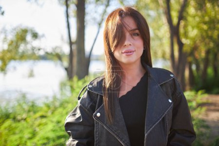 Photo for A young brunette, adorned in a leather jacket, poses against the backdrop of nature's beauty. - Royalty Free Image