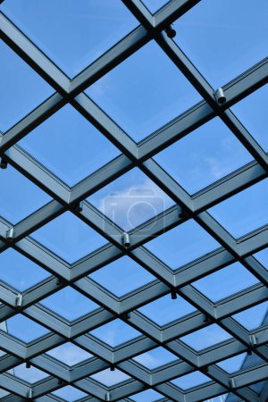 Below view of glass roof consisting of square and triangle segments with sky visible through