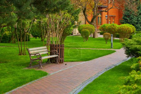 Un sentier sinueux dans le parc avec un banc à proximité, entouré d'une pelouse verdoyante, créant un espace extérieur tranquille et accueillant