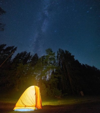 A dreamy nighttime scene with a warm yellow tent illuminated by a lantern, and the shimmering Milky Way and stars creating a serene and magical atmosphere in the background.