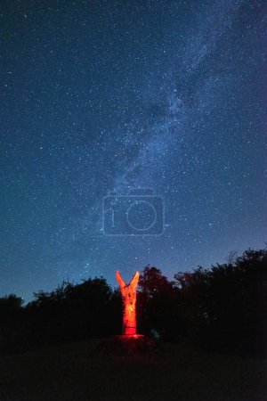 Foto de Experimente la belleza mística de estas deidades paganas talladas iluminadas por una linterna roja contra un impresionante cielo nocturno estrellado. Úsalo como telón de fondo para crear una atmósfera encantadora en tus diseños - Imagen libre de derechos