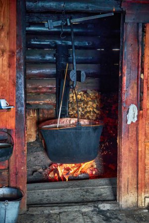Foto de Una gran cuba en la que se cocina queso sobre una fogata. El caldero negro se prepara sobre un fuego de leña abierto. Fábrica de queso en las montañas. - Imagen libre de derechos