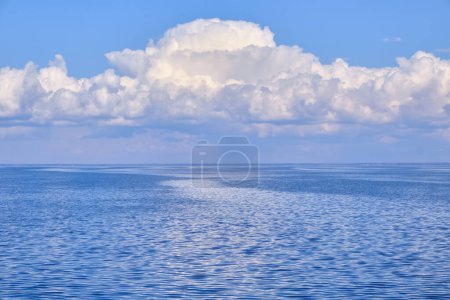 Eine ruhige Meereslandschaft mit sanften Wellen auf dem Wasser und wogenden weißen Wolken am Himmel, deren Spiegelungen auf der ruhigen Oberfläche tanzen und ein harmonisches Zusammenspiel von Licht und Natur schaffen
