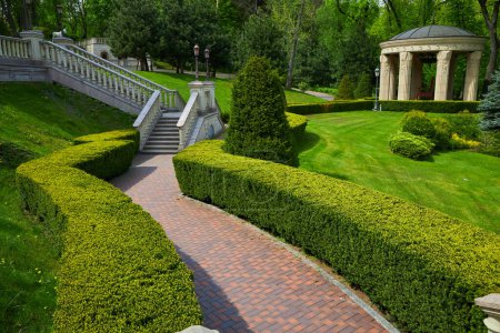 der Hinterhof des Gebäudes mit Stufen und Eingang, vor dem Sträucher immergrüner Baumarten in quadratischer Form wachsen, Fußweg aus Ziegeln um ein Labyrinth von Baumarten.