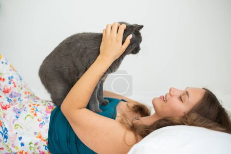 Téléchargez les photos : Jeune femme tenant doucement son chat à poil court britannique dans son lit - en image libre de droit