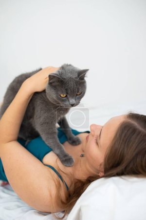 Photo for Young woman gently holding her British shorthair cat in her bed - Royalty Free Image