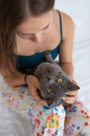 Téléchargez les photos : Jeune femme tenant doucement son chat à poil court britannique dans son lit - en image libre de droit
