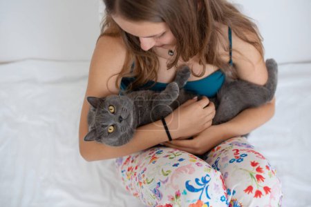 Photo for Young woman gently cradling her British shorthair cat in her bed - Royalty Free Image