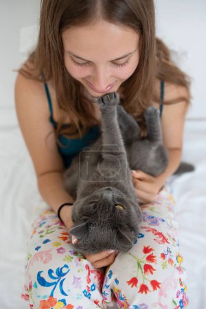 Téléchargez les photos : Jeune femme jouant avec son chat à poil court britannique dans un lit - en image libre de droit