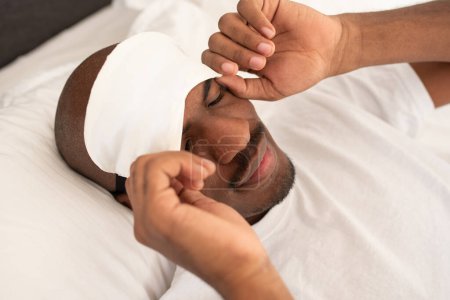 Photo for Young black man putting blindfold mask over his face before going to sleep - Royalty Free Image
