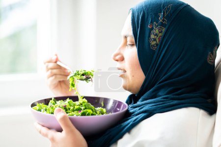Foto de Mujer musulmana con hiyab comiendo su ensalada verde sola - Imagen libre de derechos