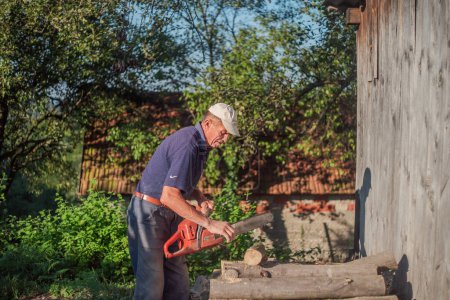 Téléchargez les photos : Homme âgé coupant un arbre avec une tronçonneuse dans le jardin. Photo de haute qualité - en image libre de droit